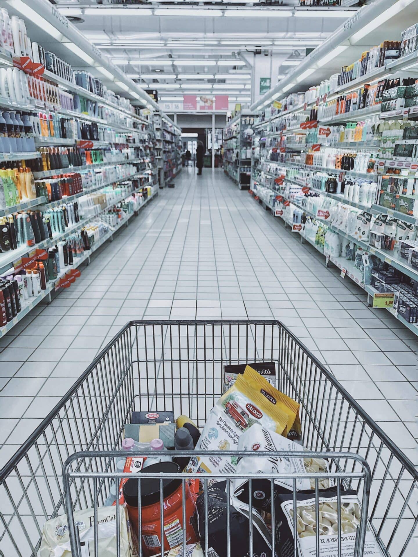 A shopping cart is filled with groceries in a supermarket aisle.